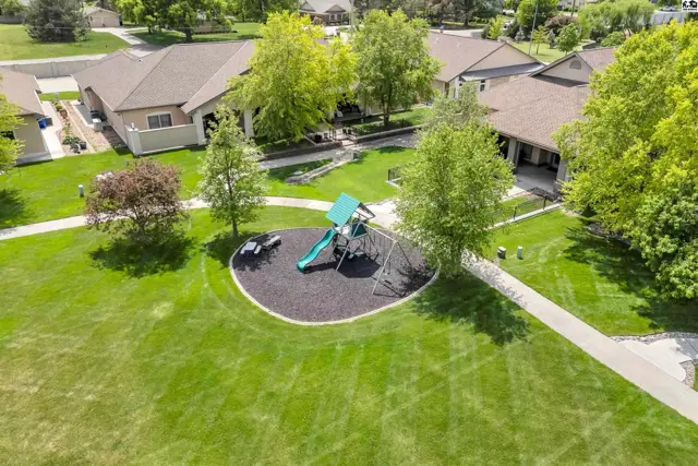 Green lawn surrounds a playground with a slide and swings, adjacent to buildings.