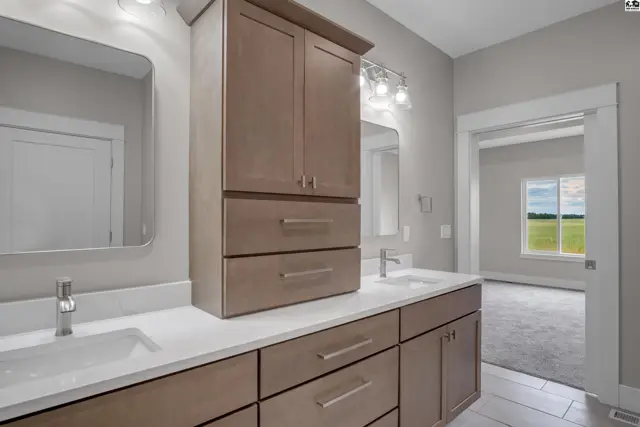 This spacious bathroom features a double vanity with a tall linen cabinet and modern fixtures.