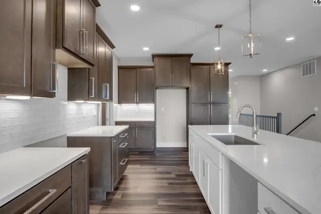 Modern kitchen features dark wood cabinetry, white quartz countertops, and stainless steel appliances.