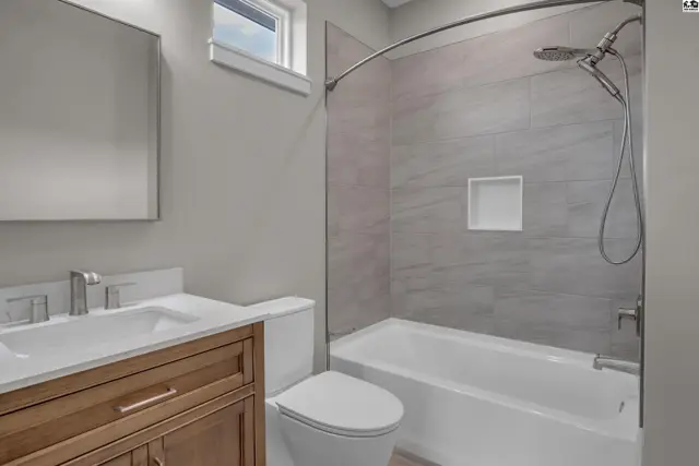 Modern bathroom features a wood vanity, white toilet, and a tiled shower-tub combination.