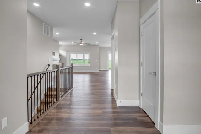 This hallway features dark wood flooring, white doors, and a railing with dark spindles.