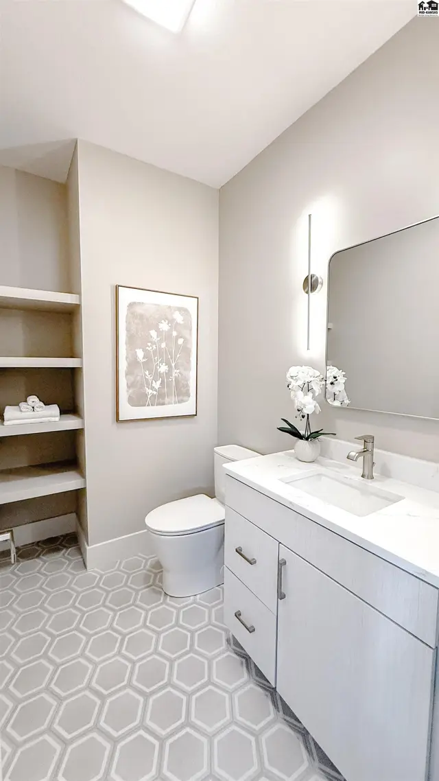 This bathroom features a vanity, toilet, and open shelving with hexagonal tile flooring.