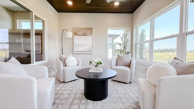 Sunlit room features white seating, a dark round coffee table, and wood-paneled ceiling.