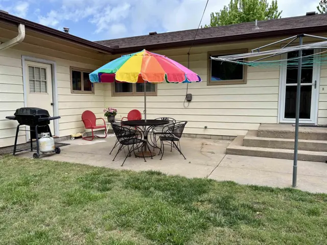 Backyard patio with a colorful umbrella, outdoor dining set, grill, and clothesline.