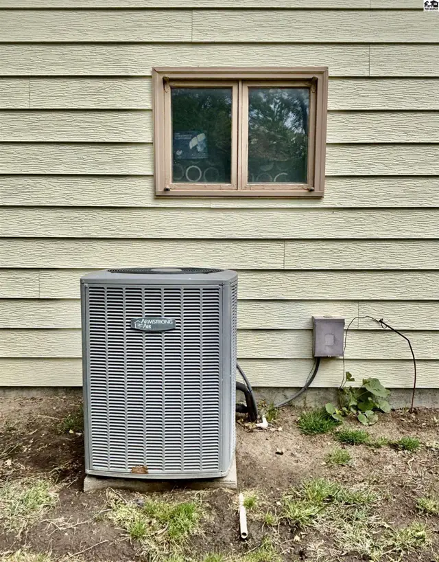 Exterior view of a light yellow vinyl-sided house with a central air conditioning unit.