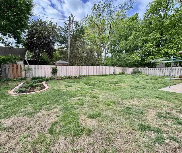 Spacious backyard with a white picket fence, mature trees, and a small garden bed.