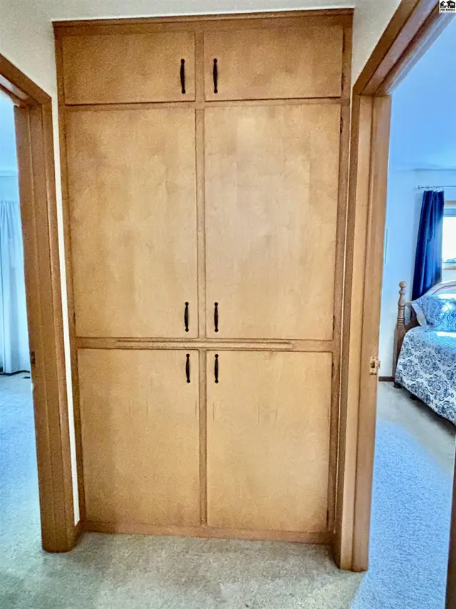 Tall, light wood built-in cabinets with dark hardware stand in a hallway, opening to a bedroom.