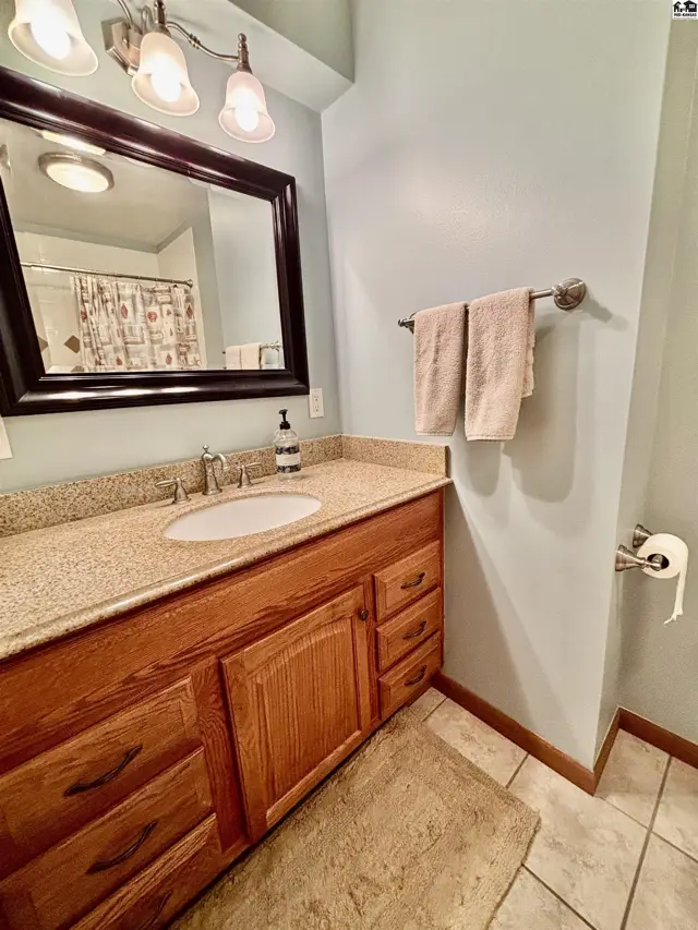 Light blue bathroom with a granite vanity, wood cabinets, and a large mirror.