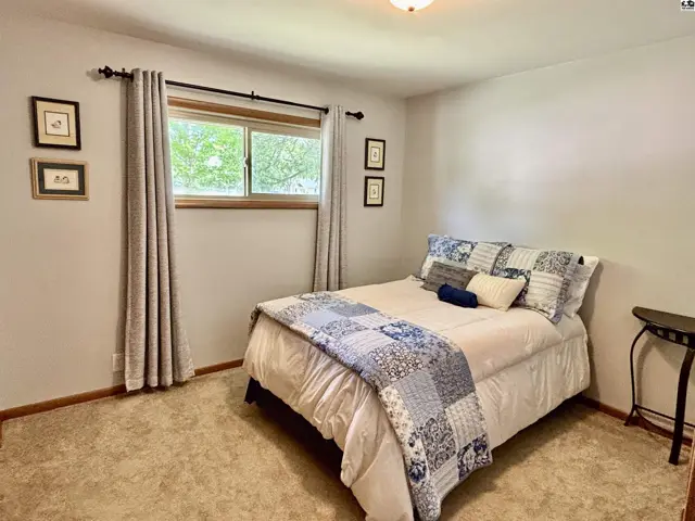 Cozy bedroom with a queen bed, blue and white patchwork quilt, and neutral carpet.
