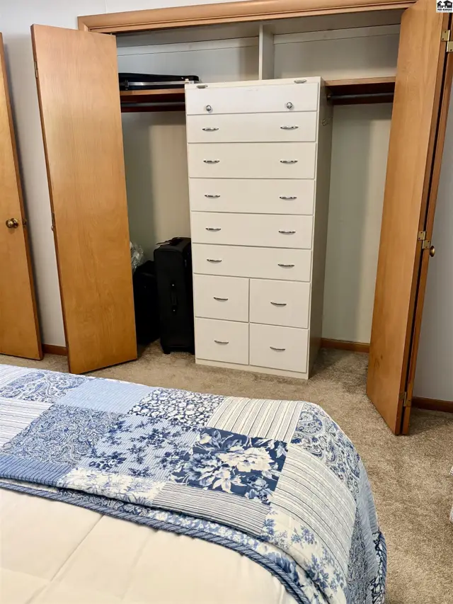 Bedroom with a tall white dresser, open closets, and a blue and white patterned quilt on the bed.