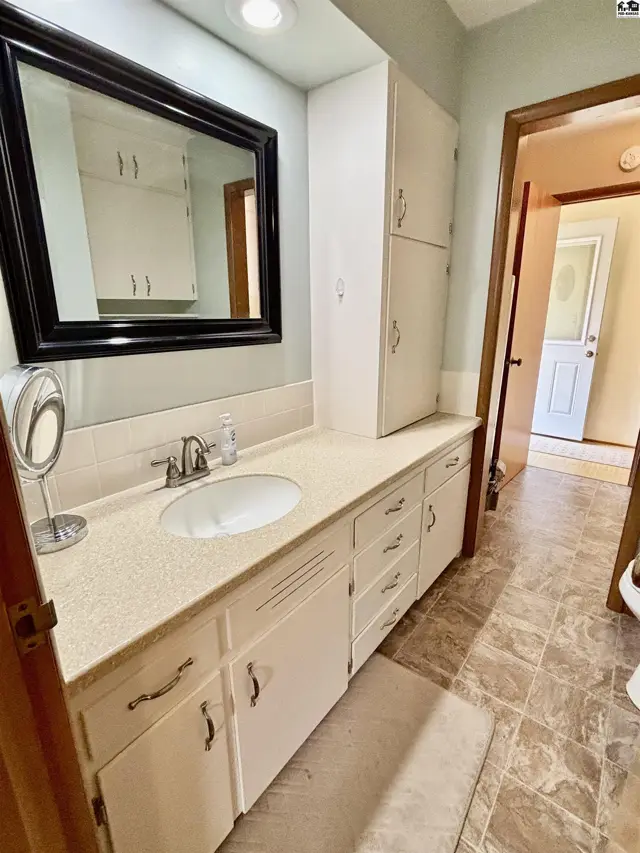 Spacious bathroom vanity with white cabinets, speckled countertop, and a large black-framed mirror.