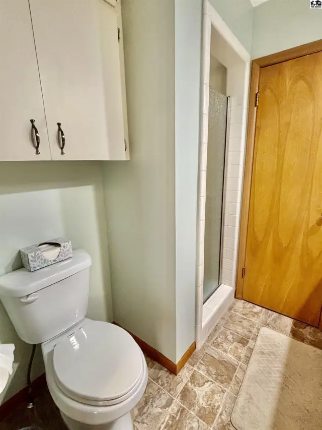 A compact bathroom features a white toilet, a glass-enclosed shower, and a light wood door.