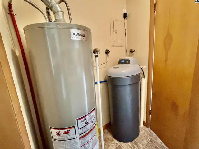 Utility room with a large water heater and water softener against beige walls and tiled floor.