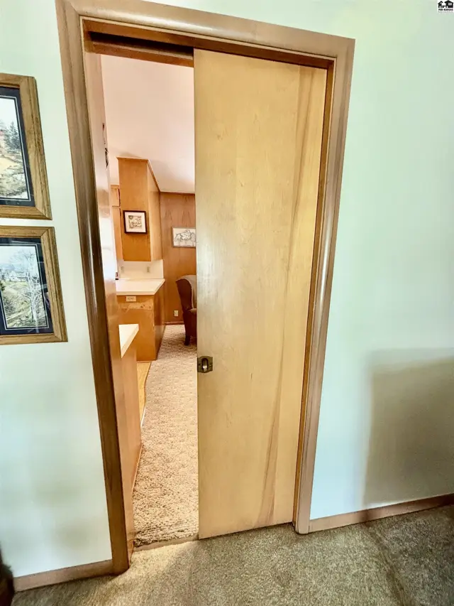 Light wood pocket door opens to a carpeted hallway and kitchen with wood cabinetry.