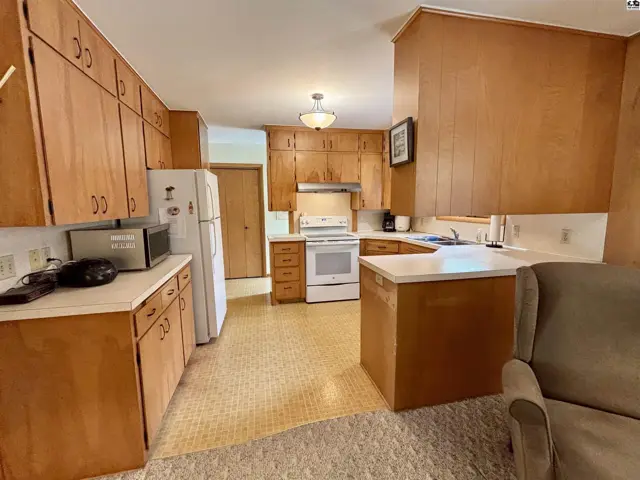 Spacious kitchen with light wood cabinets, white appliances, and a patterned floor.