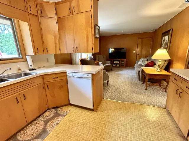 Warm wood cabinets and countertops in a kitchen open to a cozy living area with carpet.
