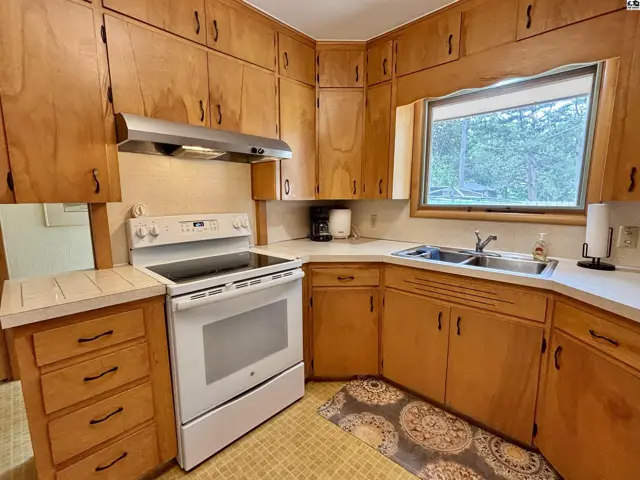 Kitchen with light wood cabinets, white appliances, and a double sink under a window.