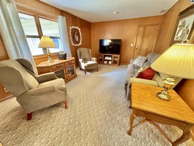 Cozy living room with plush carpet, wood-paneled walls, and comfortable seating.