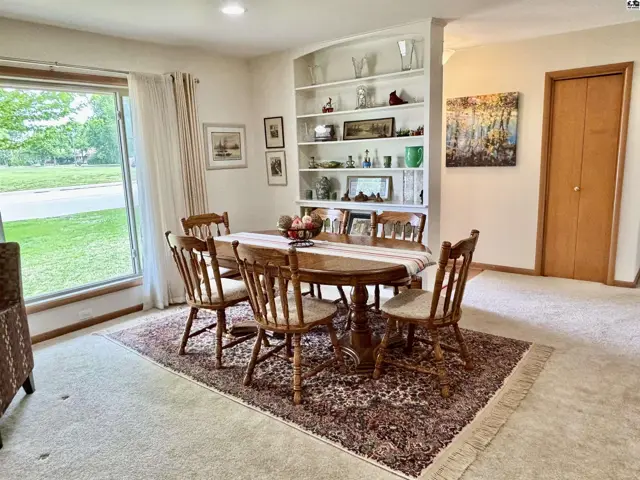 Dining room with oval wood table, six chairs, built-in shelves, and large window.