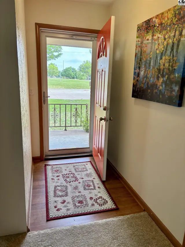 Entryway with a red-painted door, patterned rug, and artwork on a neutral wall.