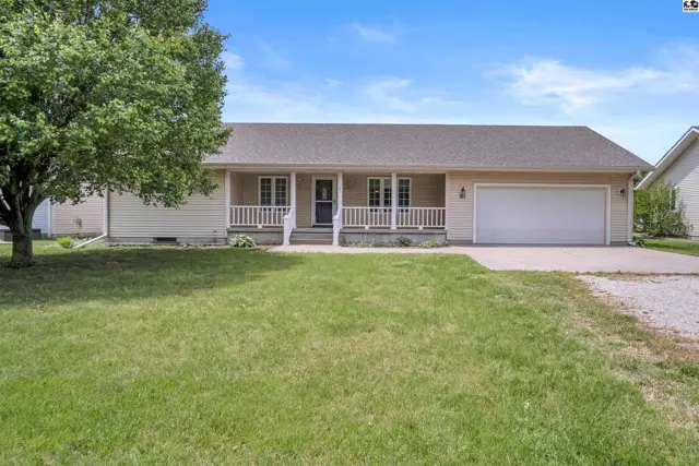 Single-story beige home with a covered front porch, white railings, and attached two-car garage.