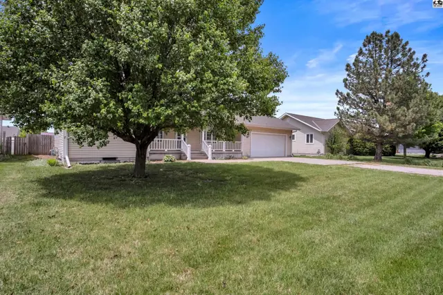 Spacious ranch home with beige siding, white trim, and a large front yard shaded by mature trees.