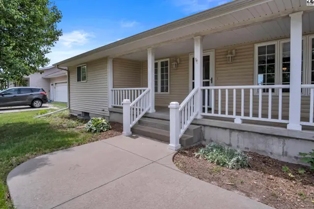 A beige vinyl-sided home features a welcoming covered front porch with white railings and stairs.