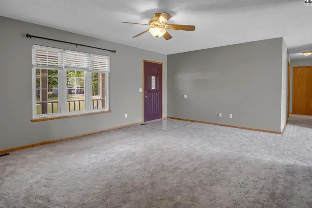 Spacious living room with gray walls, textured carpet, and a purple front door.