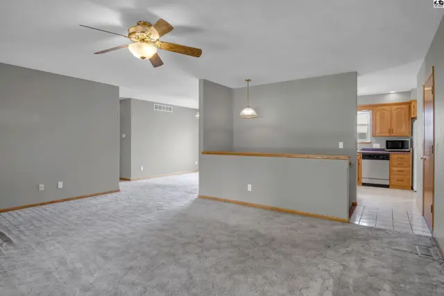 Spacious living area with gray walls, carpet, and a breakfast bar overlooking a kitchen.