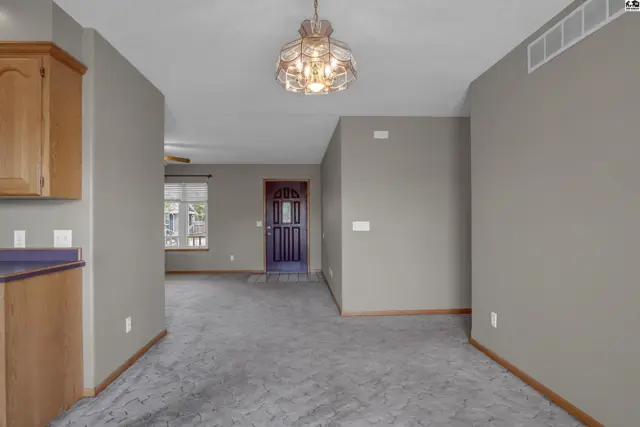 Spacious entryway with gray carpet, wood cabinetry, and a decorative chandelier.