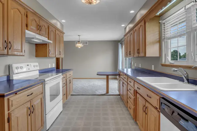 Spacious kitchen with light wood cabinets, white appliances, blue countertops, and a view into the dining area.