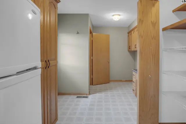 Kitchen with white appliances, light wood cabinetry, and a patterned linoleum floor.