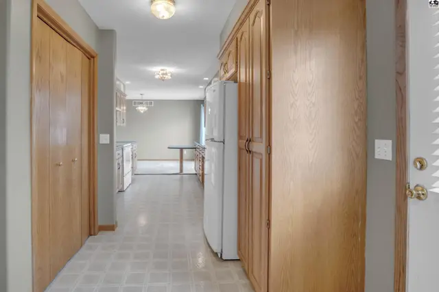 Hallway with wood cabinets, white refrigerator, and doors leading to a dining area and kitchen.