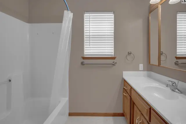 A neutral-toned bathroom features a white tub/shower combo, wood vanity with a white countertop, and a mirrored medicine cabinet.