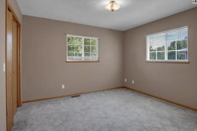 Neutral bedroom with plush carpet, two windows, and a closet with wood doors.