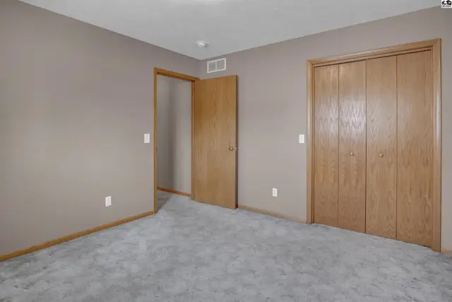 Neutral-toned bedroom with gray carpet, taupe walls, and two oak doors.