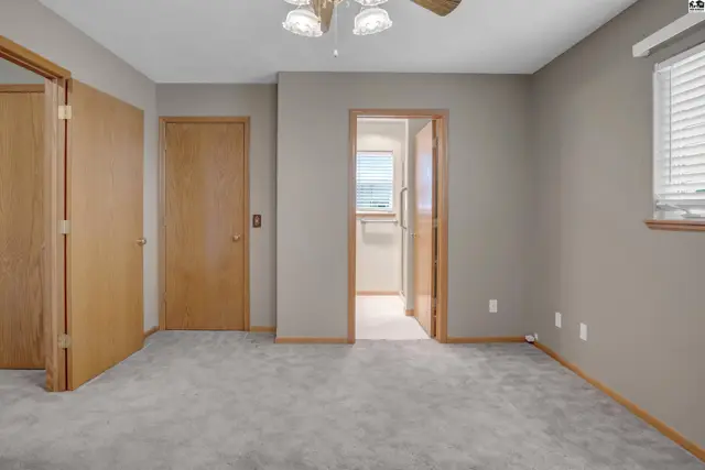 Spacious bedroom with plush gray carpet, neutral walls, and multiple wood doors.