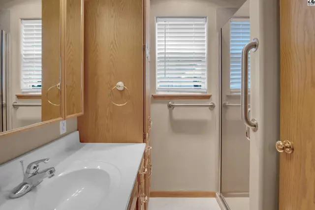 Spacious bathroom with a white vanity, wood cabinetry, and a glass-enclosed shower.