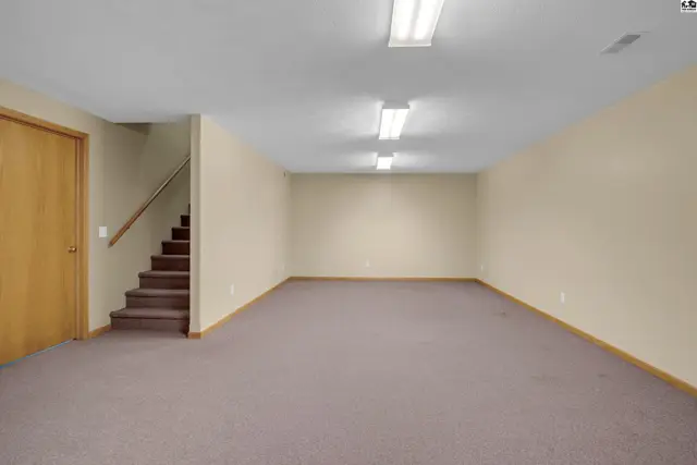 Spacious, unfinished basement with neutral carpet, beige walls, and a wooden door leading to stairs.