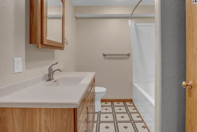 A bright bathroom with a vanity, toilet, and bathtub featuring patterned tile flooring.