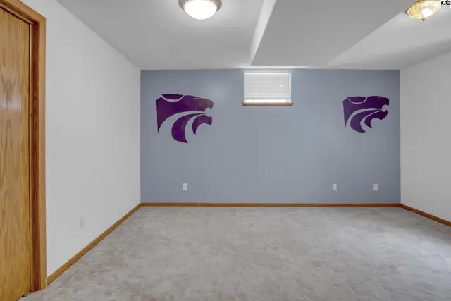 Empty room with gray carpet, light gray walls, and purple wildcat decals.