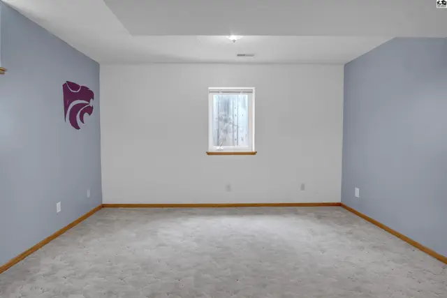 Spacious, unfinished basement room with light gray carpet, a single window, and purple accent walls.