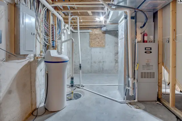 Unfinished basement with concrete walls, exposed joists, water softener, furnace, and electrical panel.