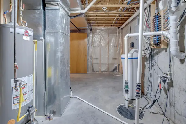 Unfinished basement with concrete floors, exposed joists, water heater, and plumbing.