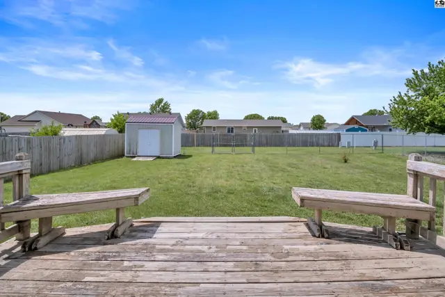 Spacious backyard with a wooden deck, benches, and a storage shed under a clear blue sky.