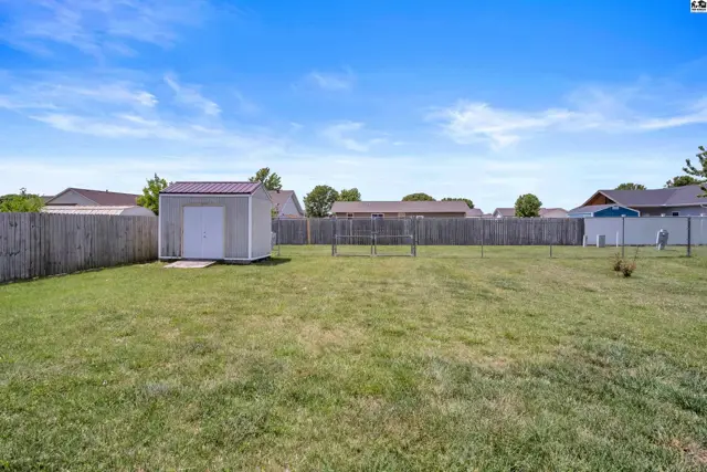 Spacious, fenced backyard with a storage shed and clothesline under a bright blue sky.