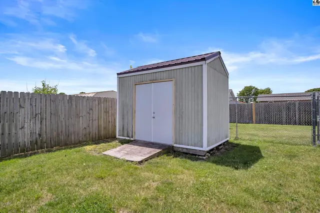 A light green shed with a metal roof sits on a concrete foundation in a grassy backyard.