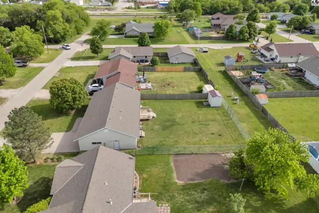 Aerial view of suburban homes with fenced yards, mature trees, and a paved street.