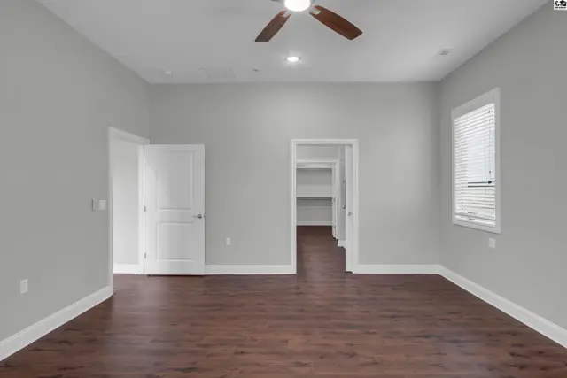 Spacious room with hardwood floors, a ceiling fan, and a walk-in closet.