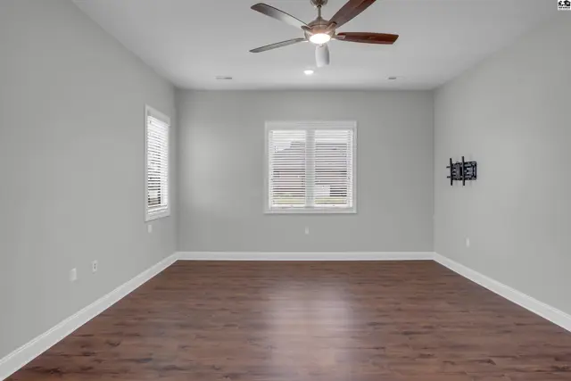 Spacious room with hardwood floors, ceiling fan, and wall-mounted television bracket.